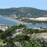 Vista panorâmica da Lagoa da Conceição em Florianópolis, com montanhas, vegetação e espelho d’água ao entardecer