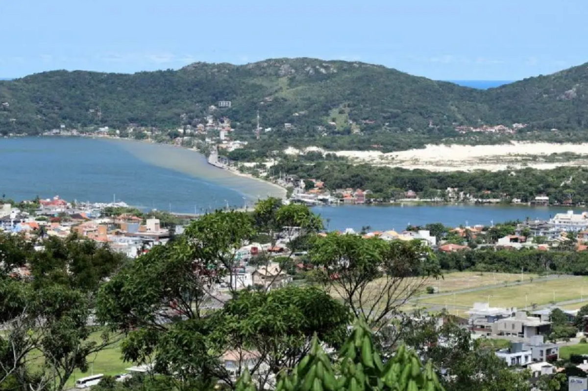 Vista panorâmica da Lagoa da Conceição em Florianópolis, com montanhas, vegetação e espelho d’água ao entardecer